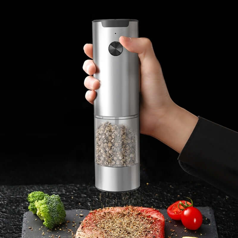 Electric salt and pepper grinder being used to season fresh vegetables and steak, showcasing its sleek design.