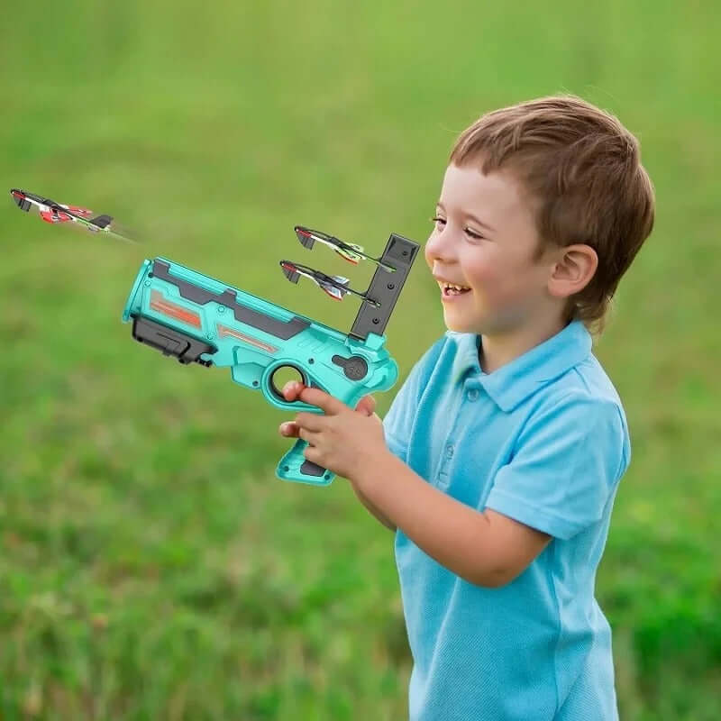 Smiling child playing with Airplane Launcher Blaster Toy, launching foam glider planes outdoors.